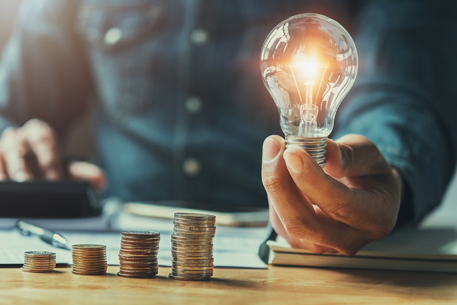 business man hand holding lightbulb with using calculator to calculate and money stack. idea saving energy and accounting finance in office concept