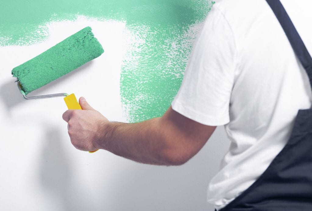 Close-up of worker with roller painting white wall on green