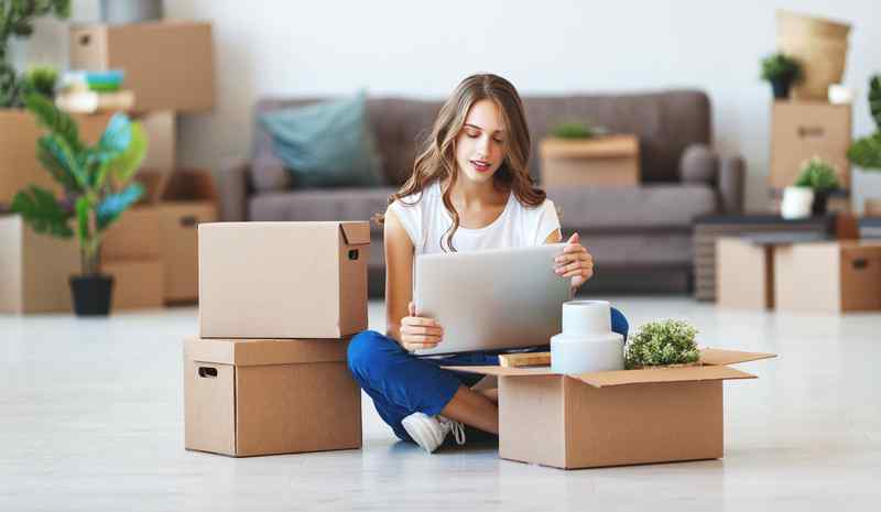 happy young girl with boxes moves to new apartment