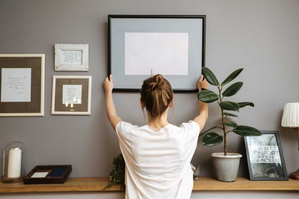 Girl hanging a frame on a gray wall, sun light