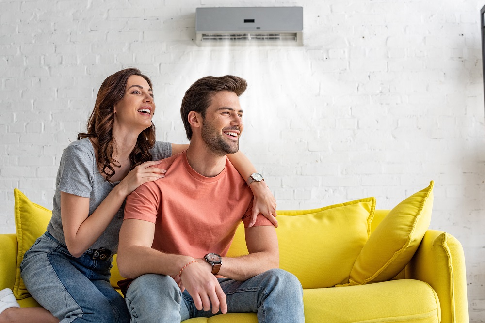 cheerful couple sitting on yellow sofa under air conditioner at home