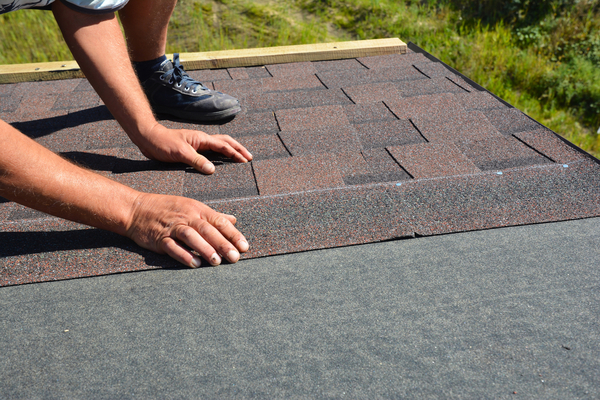 Roofer hands laying Asphalt Shingles on house construction roof.