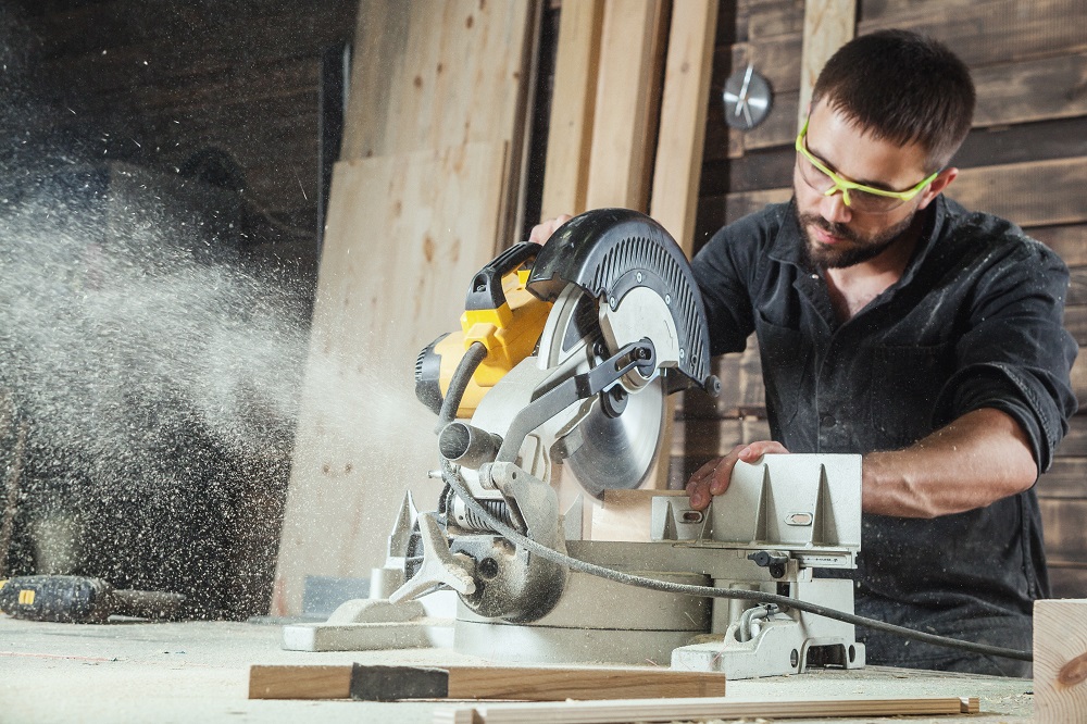 Close-up as a young male construction worker carpenter saws a circular saw blade, sawdust fly in the workshop