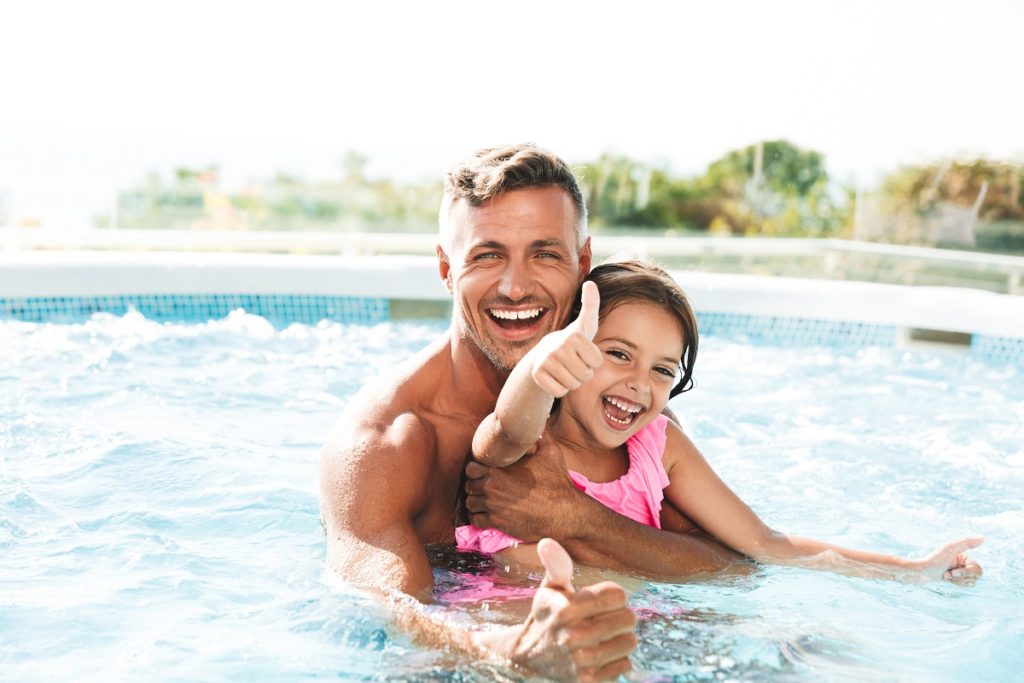 Photo of happy family father with daughter smiling, while swimming in pool outdoor during summer vacation