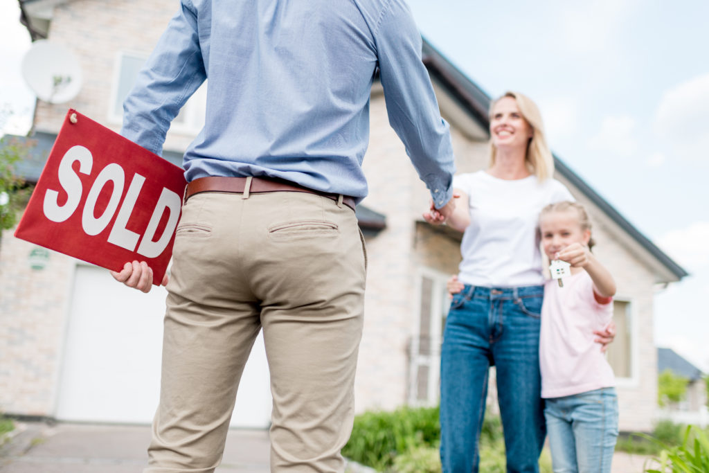 cropped shot of realtor with sold sign shaking hand of young wom