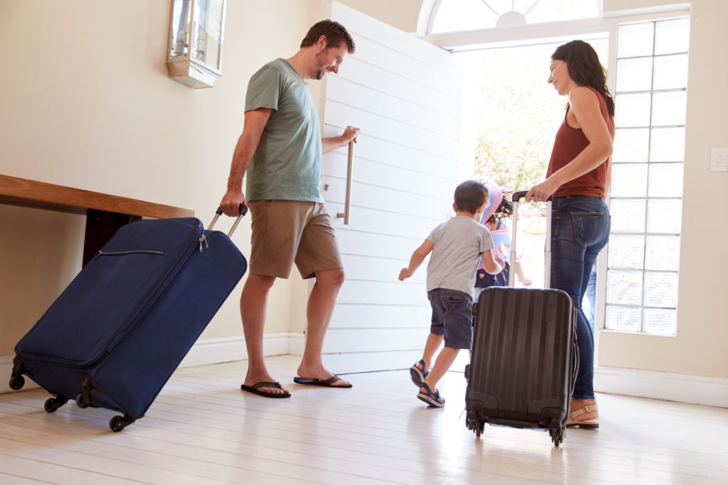 Mid adult white couple and kids leaving their home with luggage to go on vacation, full length