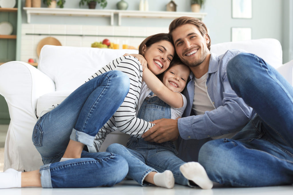 Young Caucasian family with small daughter pose relax on floor in living room, smiling little girl kid hug embrace parents, show love and gratitude, rest at home together.