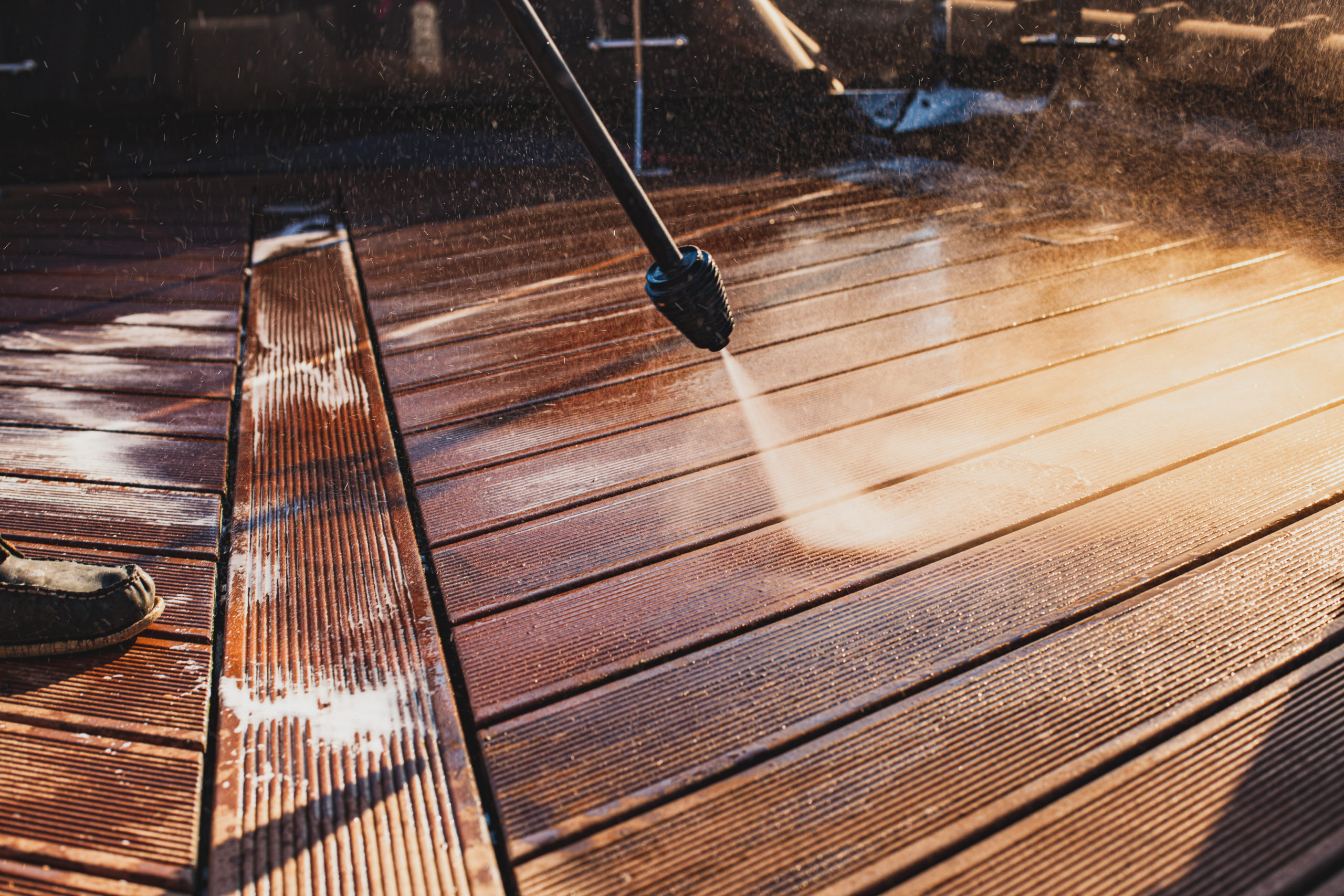 man cleaning terrace with a power washer – high water pressure cleaner on wooden terrace surface
