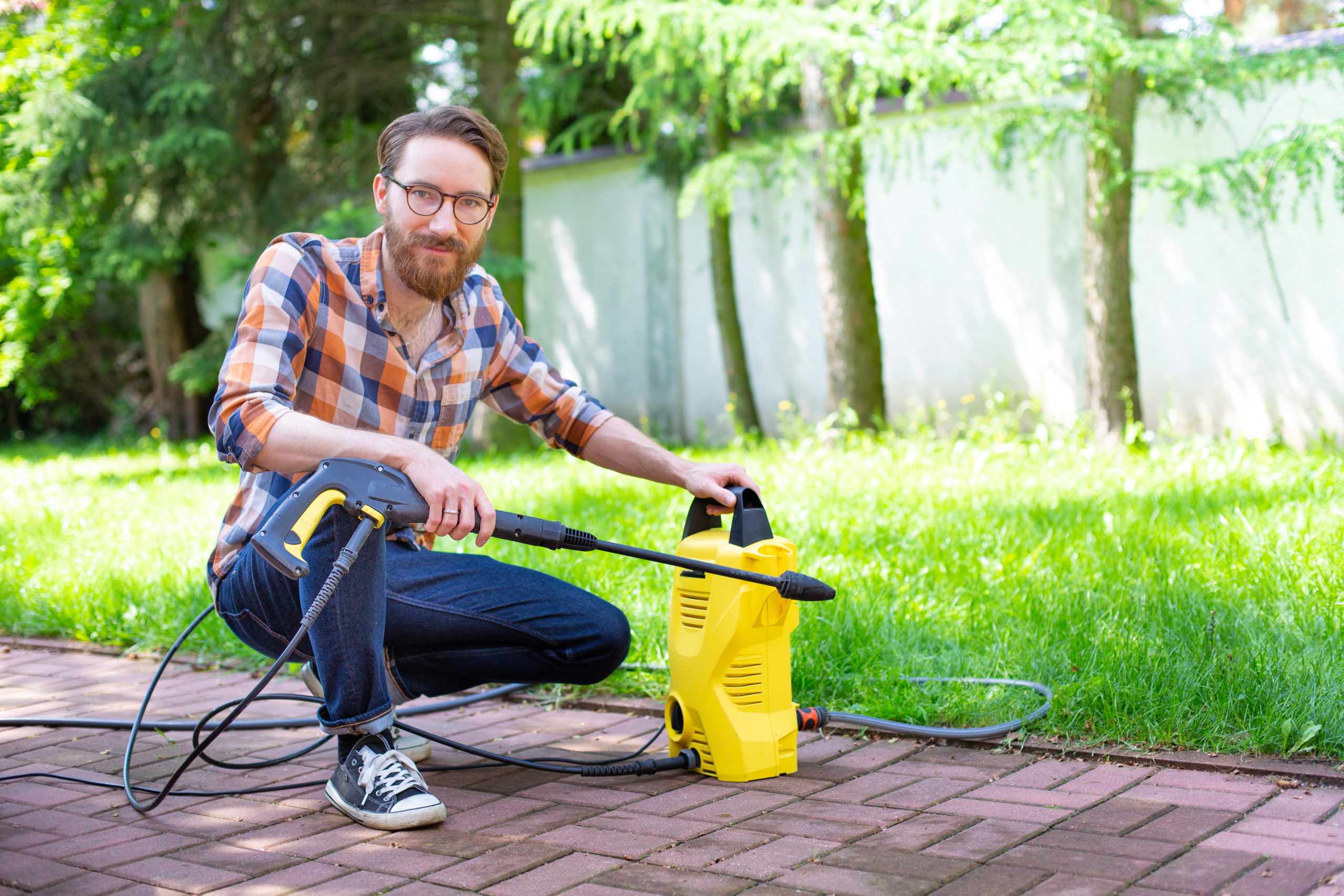 Man using a high pressure washer in the backyard, on a sunny day.