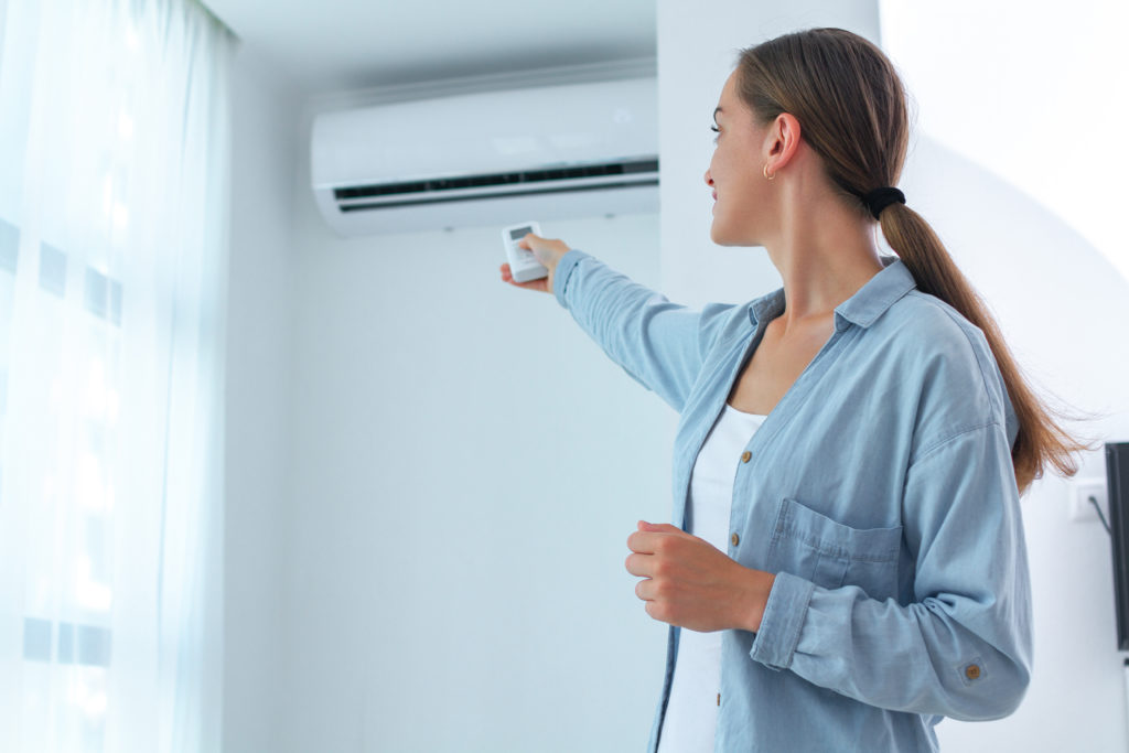 Young woman adjusts the temperature of the air conditioner using