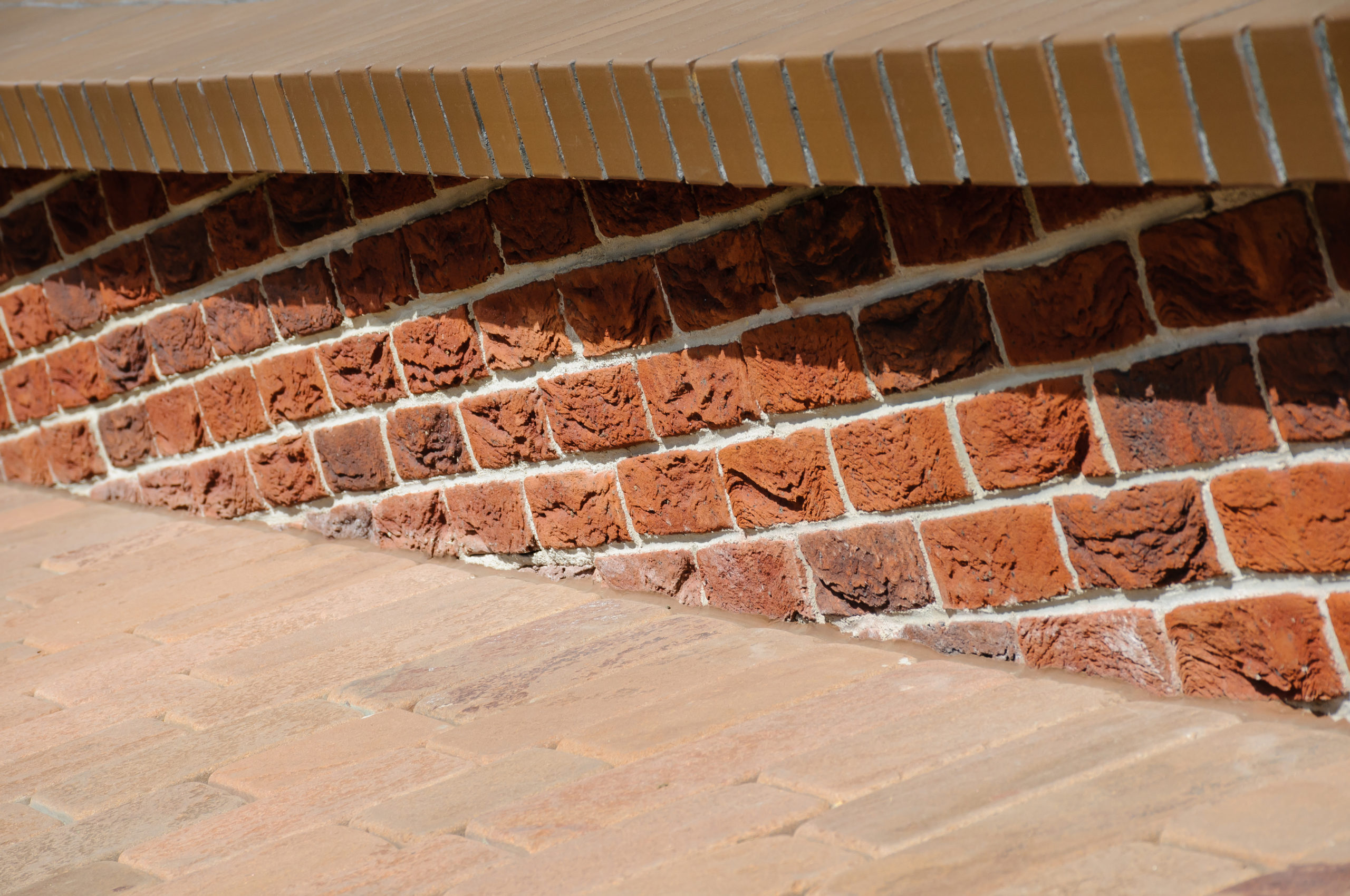 Low parapet made of raised red and dark red bricks beside brick pavement