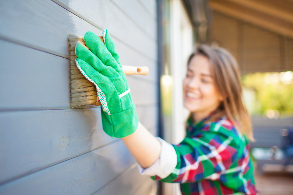 Cheerful woman applying protective varnish or paint on wooden ho