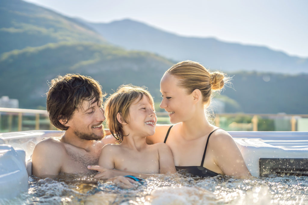 Portrait of young carefree happy smiling happy family relaxing at hot tub during enjoying happy traveling moment vacation. Life against the background of green big mountains