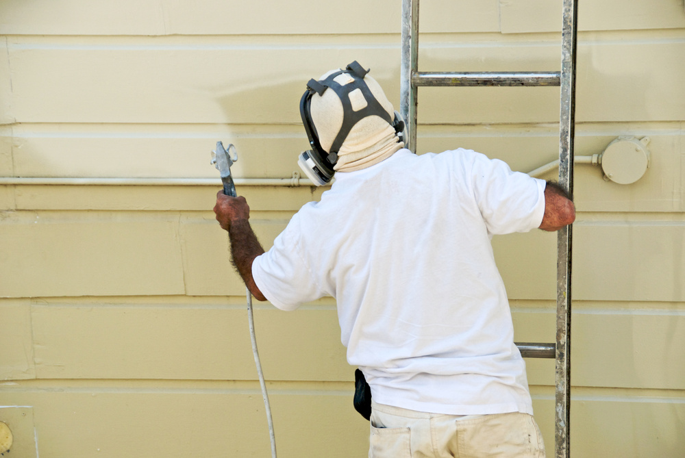A man on a ladder uses paint spray gun