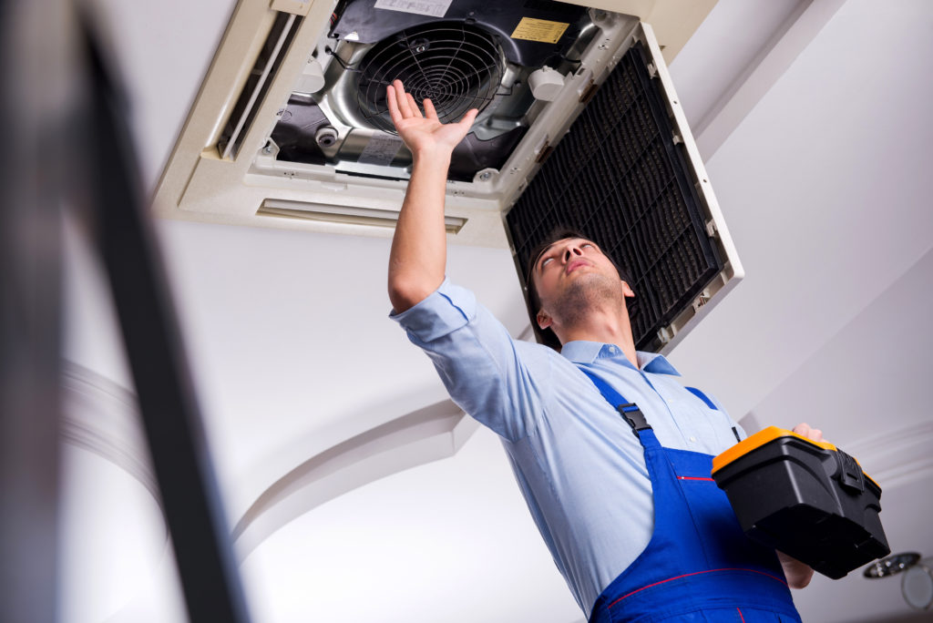 Young repairman repairing ceiling air conditioning unit