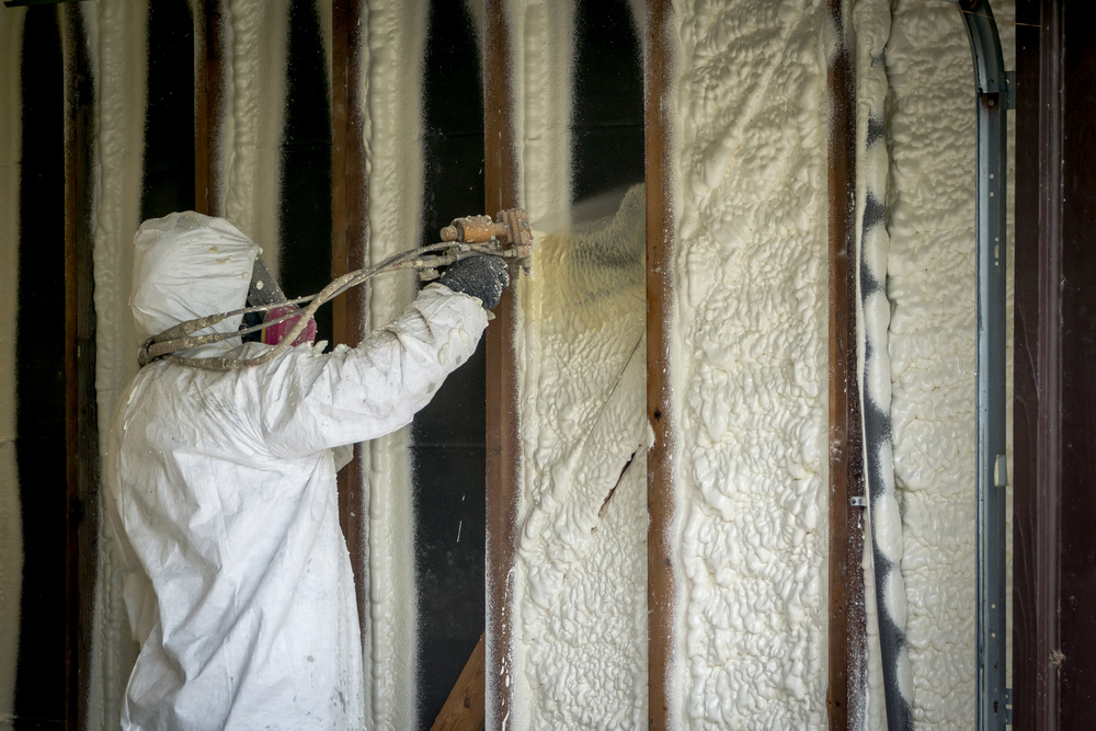Worker spraying closed cell spray foam insulation on a home that