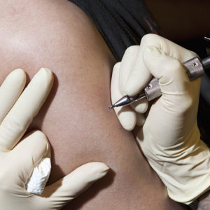 A tattoo artist preparing to tattoo a man’s bare arm, close-up