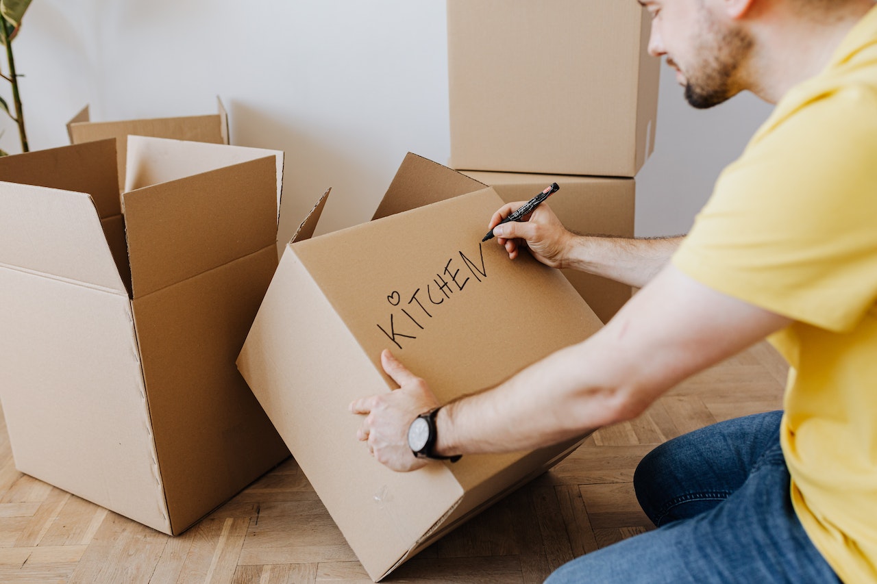 Man labeling a box by writing 'kitchen' on it