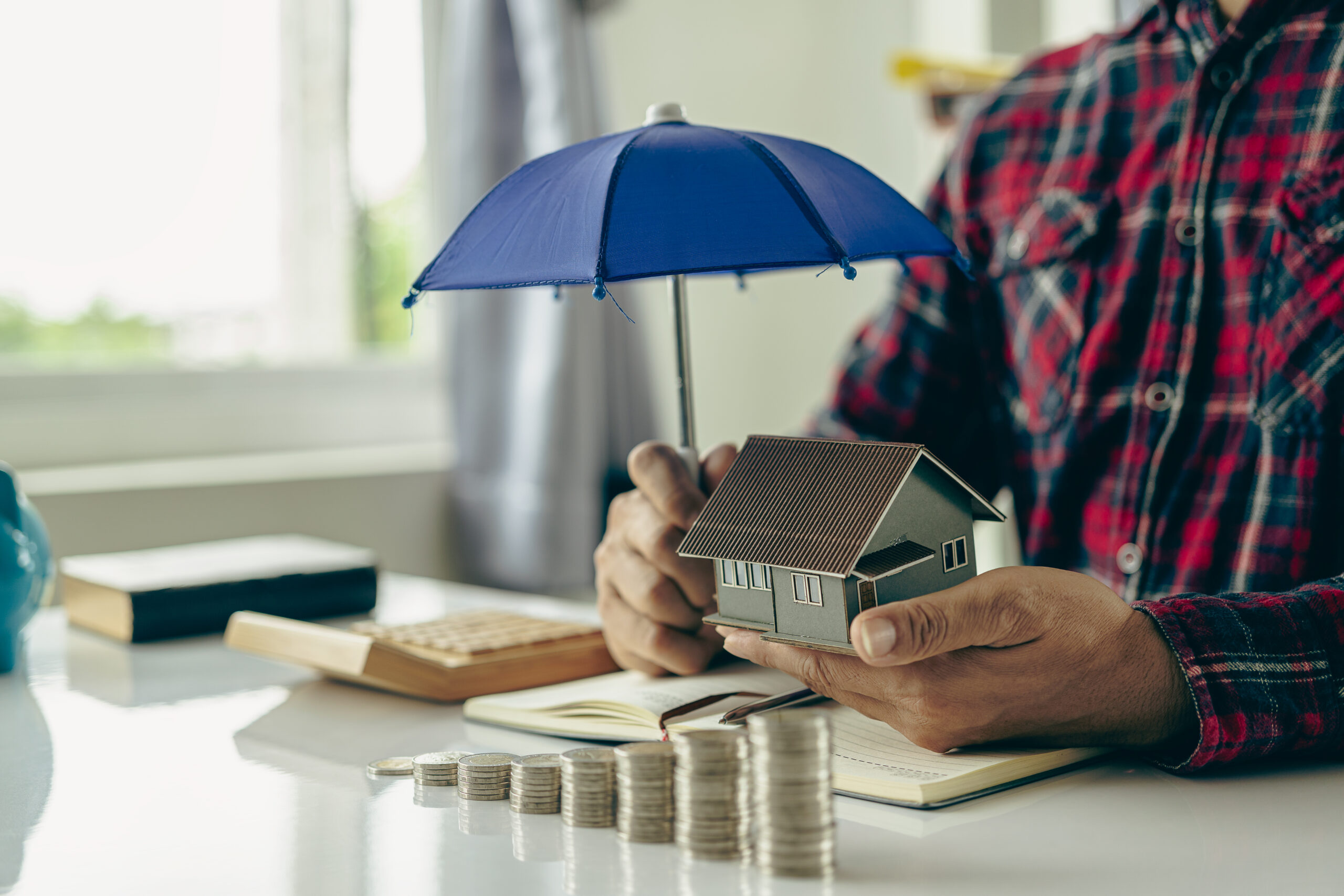 Man holding a blue umbrella and a house Insurance agent holds blue umbrella over modern house model Property insurance Home insurance concept Close-up pictures