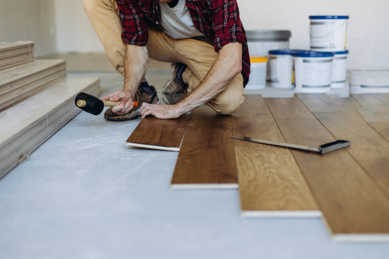 Installing the parquet floor, a man hands fixing one tile with a hammer