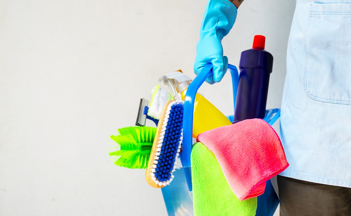 Man holding mop and plastic bucket with brushes, gloves and detergents in the kitchen